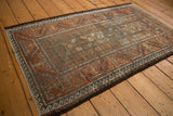 Distressed Belouch rug side: rust, blue, brown meandering vine and wave borders.