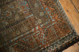 Distressed Belouch rug corner, featuring meandering vine border, rustic brown, sky blue, and rust.