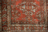 Distressed brick red and slate repeating patterns in the Belouch rug border.