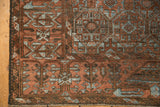 Textured corner of a distressed Belouch rug showing terracotta and slate blue geometric patterns with fringe.