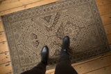 Distressed vintage Belouch rug featuring faded rams horn and starburst motifs in beige and charcoal.