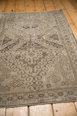 Vintage Belouch rug corner with distressed beige field and muted charcoal geometric border.