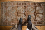 Distressed vintage Belouch rug runner with abrashed brown ground and geometric gul motifs.