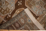 Distressed Belouch rug corner showing geometric brown gul patterns, hand-knotted back, and beige selvage.