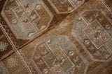 Distressed pile of a vintage Belouch rug, featuring abrashed brown ground and geometric gul motifs.
