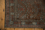 Distressed Belouch rug corner, slate blue and brick red geometric patterns, worn knot heads.