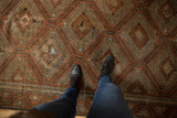 Underfoot view of a distressed vintage Belouch carpet, featuring geometric medallions in terracotta and slate blue.