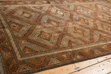 Distressed Belouch carpet corner with geometric hook and latch motifs in terracotta and brown.