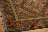 Distressed Belouch carpet corner showing geometric medallions and hook motifs in terracotta and brown hues.