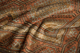 Folds highlighting the lustrous, distressed pile of a Belouch rug with geometric hook motifs in terracotta and blue.
