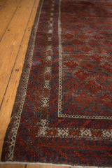 Distressed vintage Belouch rug corner; ruby red, sapphire blue patterns, lustrous pile, even wear.