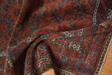 Textured folds of a distressed Belouch rug, showcasing cherry red, sapphire blue, and ivory guls.