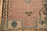 Distressed Belouch rug corner showing faded dusty rose pile and geometric beige and blue motifs.