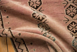 Abrashed dusty rose pile of a distressed Belouch rug with floral gul medallions.