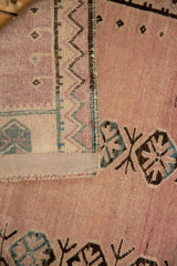 Distressed Belouch rug pile in dusty rose and charcoal, with geometric hand-knotted foundation.