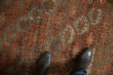 Geometric guls and lattice vinery in rust, charcoal, slate blue, and ivory on the distressed rug, with boots.
