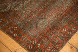 Distressed vintage Belouch rug corner, featuring madder red border, ivory floral motifs, and visible knot-head wear.