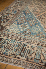 Distressed pile of a vintage Joshegan rug, showing blue and beige garden motifs.