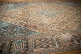 Distressed vintage Joshegan carpet showing dark brown geometric border and worn field patterns.