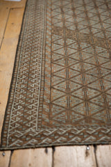 Worn vintage Belouch rug corner, revealing lattice motif and reciprocating wave border in brown, ivory, and blue.