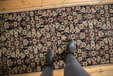 Feet on a distressed Karabagh runner, revealing intricate Herati motif in navy, ivory, and rose.