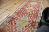 Distressed red Oushak runner with geometric hook and latch motifs and floral cross-section border.