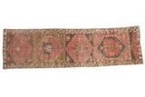 Distressed Oushak runner rug displays geometric medallions in dusty rose and charcoal colors.