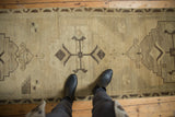 Distressed vintage Oushak runner featuring abrashed beige field with primitive charcoal motifs.