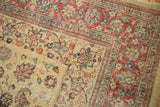 The worn corner of a vintage Tabriz rug with red and blue scrolling vinery over a pale gold field.