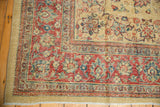 Corner of a distressed Tabriz carpet with cherry red and blue floral borders against a pale gold field.