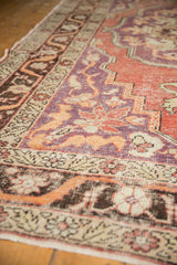Worn low-pile texture on a distressed Oushak carpet corner with violet, red, and sand floral motifs.