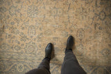 Feet on vintage distressed Oushak rug, emphasizing worn ivory and muted blue floral pattern.