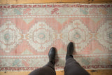 Distressed vintage Oushak runner with muted dusty rose, seafoam, and faded orange motifs underfoot.