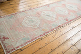 Distressed Oushak runner with intact side selvage, worn pile, and faded geometric rose border.