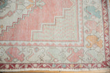 Corner of distressed Oushak runner with pale blush field, geometric spandrel, and worn pile texture.