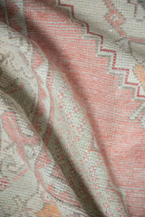 Folded Oushak rug revealing textured pile, muted dusty rose, and seafoam green tones.