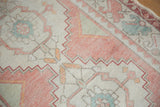 Distressed Oushak rug showing faded dusty rose and seafoam green geometric floral details.