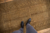 Muted gold and brown distressed Turkmen rug, showing geometric patterns, even wear, and boots.