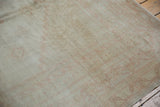 Corner of vintage distressed Oushak rug with softly worn ivory and pale blush patterns.
