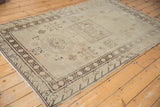 Distressed Khotan rug close-up: charcoal geometric border, faded field, and visible foundation.