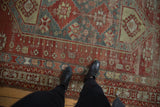 Distressed vintage Caucasian carpet displaying lozenge medallion, pinwheel motifs, and faded cherry red and denim blue tones.
