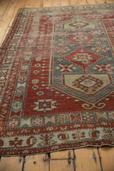 Distressed cherry red and denim blue geometric patterns on a vintage Caucasian carpet.