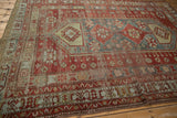 Distressed Caucasian carpet corner with worn cherry red field, pinwheel, and denim blue geometric borders.