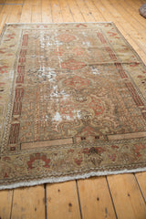Distressed vintage Malayer rug corner, showing neutral floral patterns and exposed foundation.