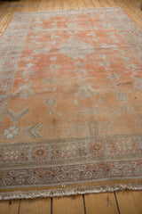 Distressed Khotan carpet's burnt orange pile, intricate silver and ivory geometric border, and cream fringe.