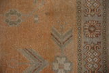 Distressed Khotan carpet close-up: burnt orange field, geometric silver-grey motifs, and patterned border.