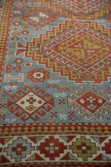 Distressed vintage Caucasian rug with geometric brick red and gold motifs on slate blue.