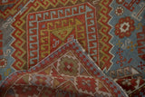 Folded vintage Caucasian rug displays distressed brick red, slate blue, gold geometric pile, hand-knotted.