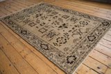 Angled view of a distressed Malayer rug with interconnected starburst motifs in sand and brown.