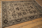 Vintage distressed Malayer rug shown from an angle, with geometric starburst designs on a sand-colored field.